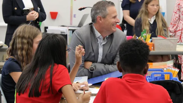 A man in a gray suit sits among children