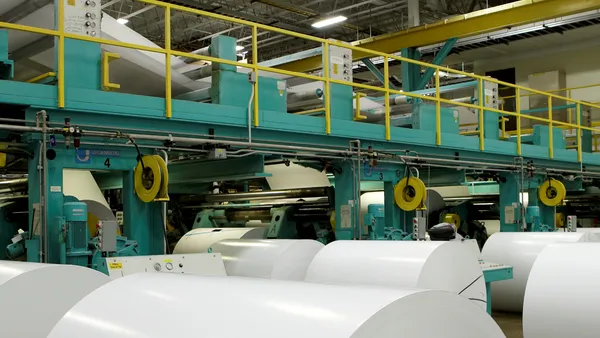 Large rolls of paper are lined up in an industrial facility.