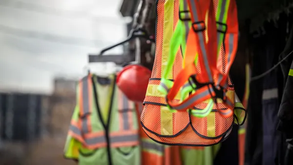 Bright construction vests and gear hang on a rack near a jobsite.