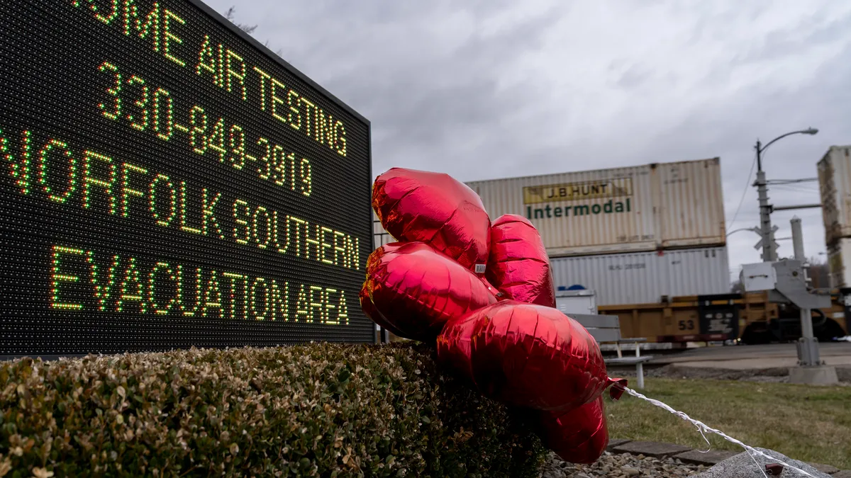 Red balloons are seen next to a digital sign saying residents can receive air-quality tests from Norfolk Southern Railway. In the background, shipping containers can be seen on a train.