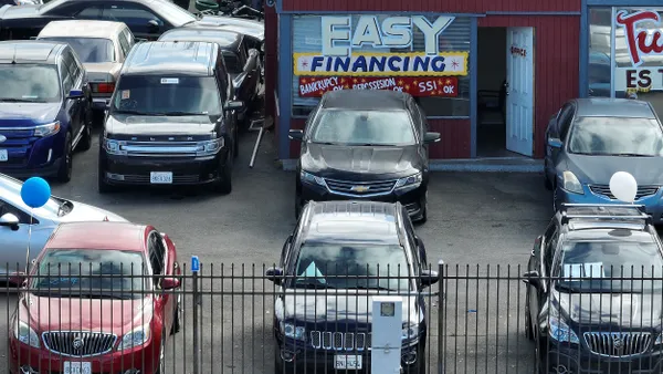 Cars parked at a used car lot with a sign on the window of a building that reads,"Easy Financing."