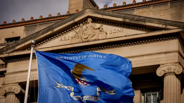 A blue flag that says "Department of Justice" waves in front of the agency's building.