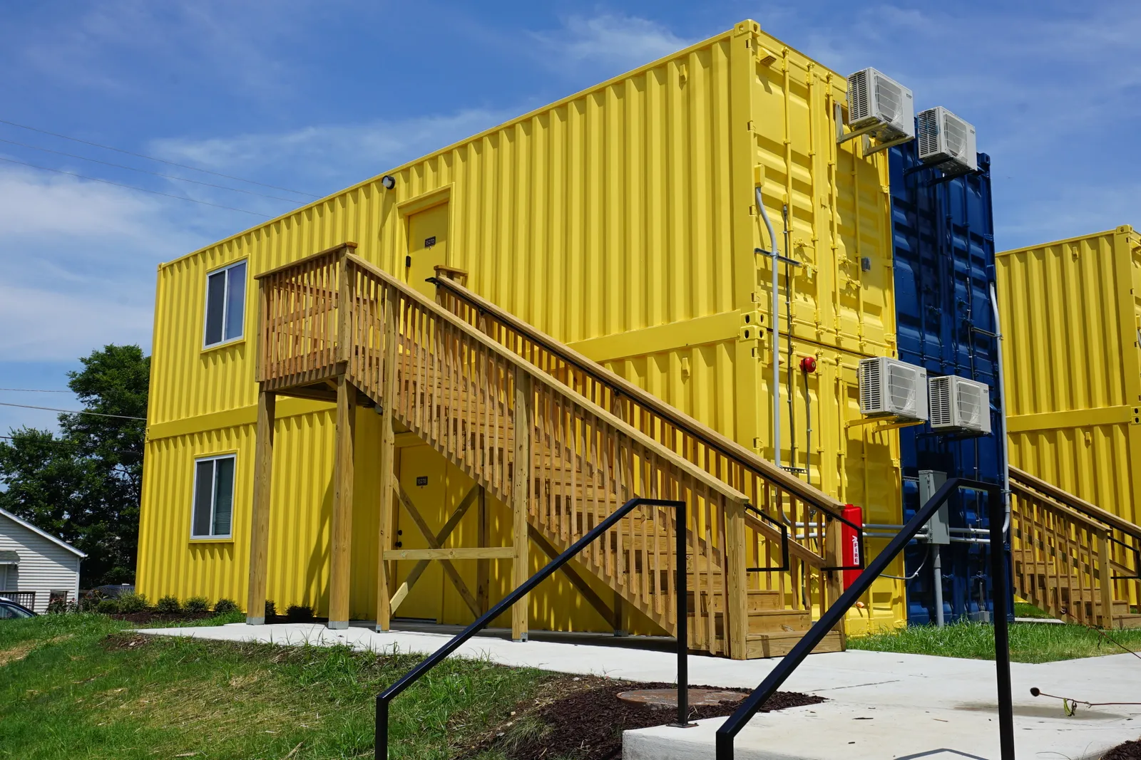 A stack of two shipping container apartments with a wooden staircase leading to the second floor.