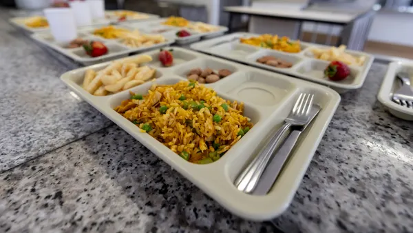 A close-up of a tray of food with rice, fruit, beans a fork and a knife.