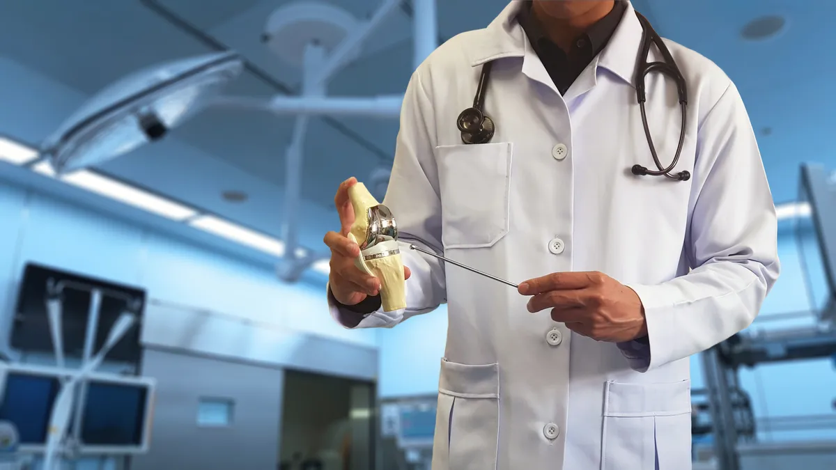 A man in surgical garb holds a replacement knee joint