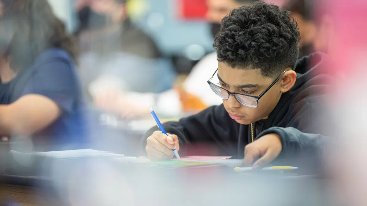 High school student works at desk in classroom with pen in hand.