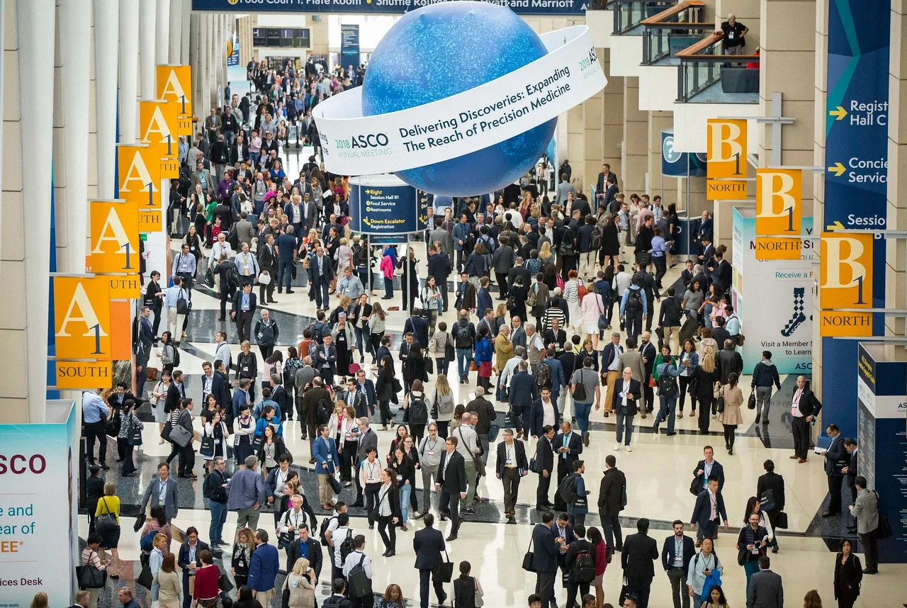 People walk through the main hall of a convention center during a cancer research conference.