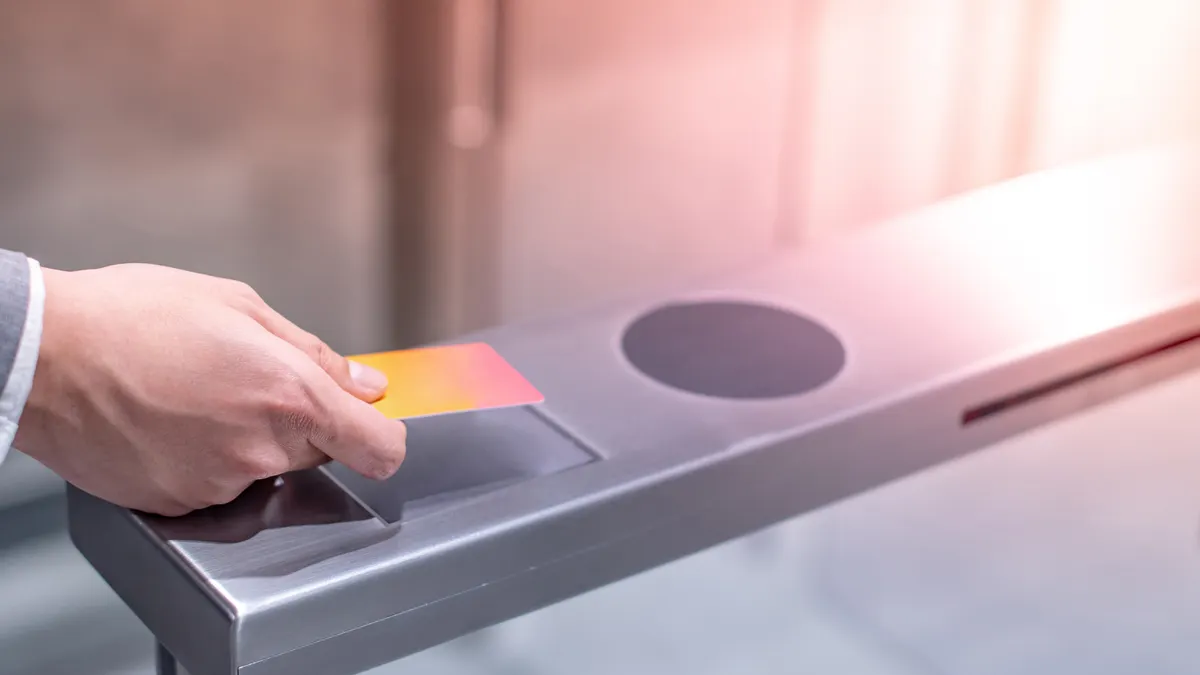 A closeup shot of the hand of a businessperson using an orange smart card to open an automatic gate machine in an office building.