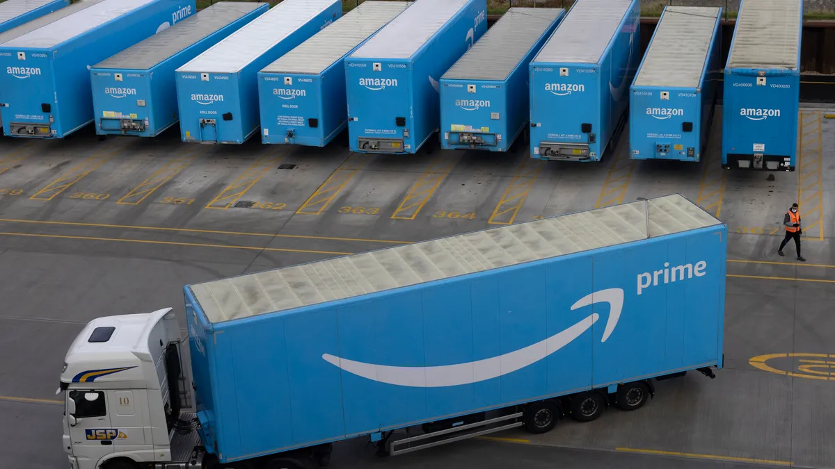 A blue delivery truck with the Amazon logo on the side pulls out of a warehouse