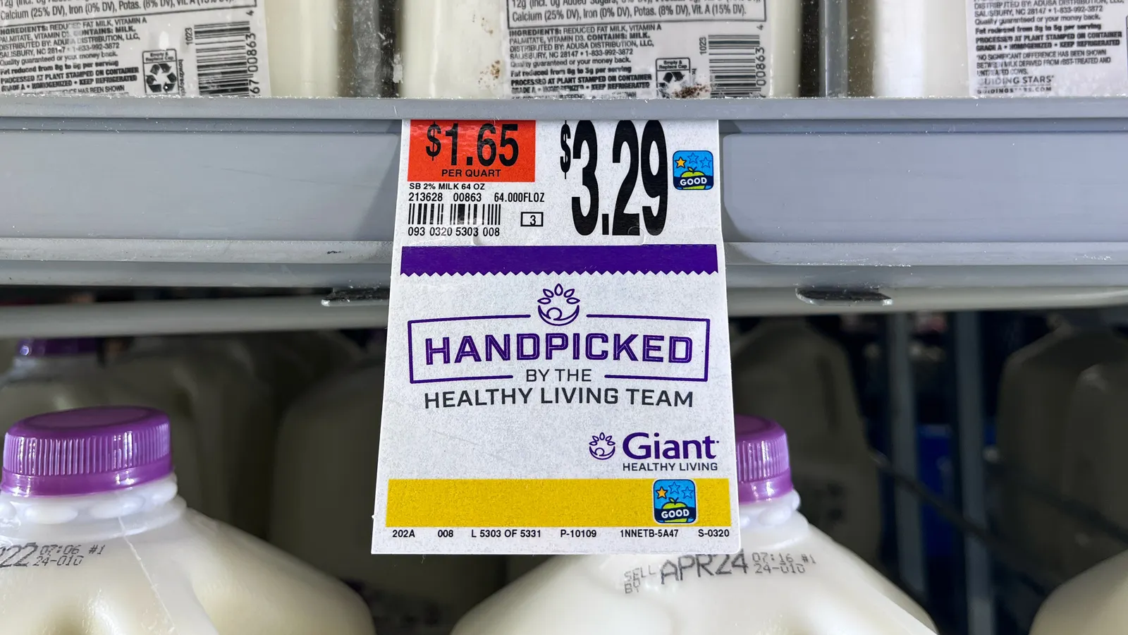 A price tag on a supermarket shelf that says “$3.29” and “Handpicked by the Healthy Living Team” beneath containers of reduced fat milk.