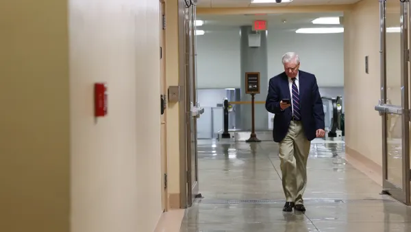 A person wearing a blue suit and red tie walking through a hallway and looking at phone.