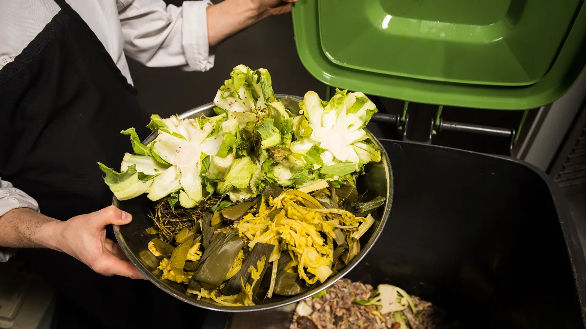 An image of a chef disposing vegetable waste into a composting bin.