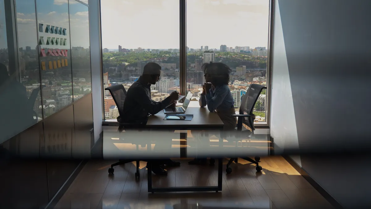 Two people talk in a conference room.