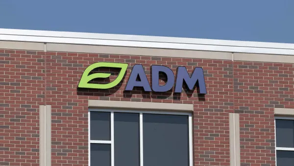 A close-up view of a red brick building with a large "ADM" logo mounted near the roofline, featuring a green leaf icon and dark blue letters.