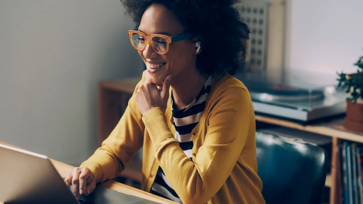 Black woman sits smiling with laptop at her desk