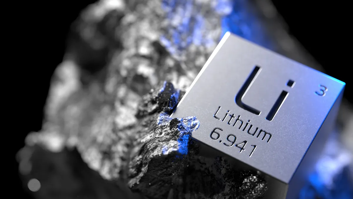 A silver block with Li on the front tilted to right, laying on top of a dark gray rock.