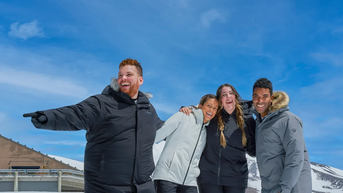 Four happy people stand in snow wearing Moosejaw apparel.