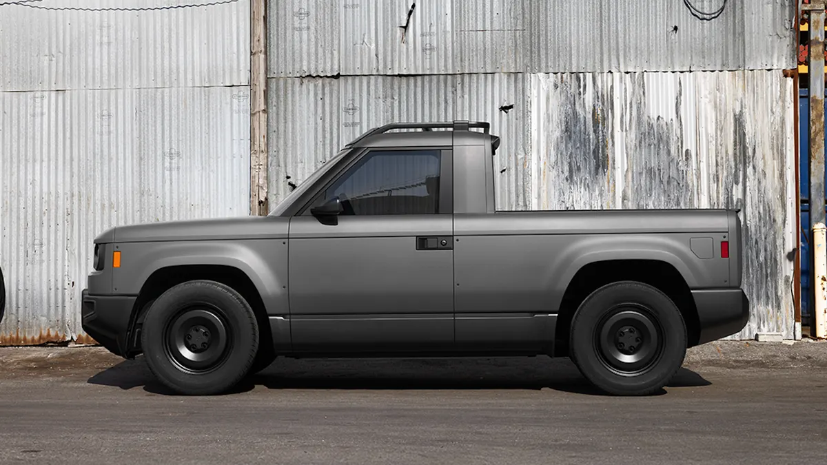 A gray Slate Auto electric truck parked outdoors in front of an industrial building with metal siding.