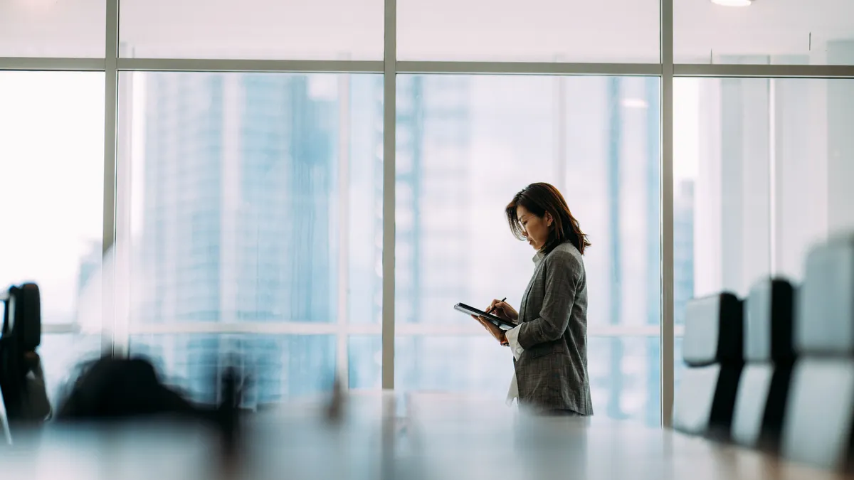 an executive in business attire reads from a tablet in a meeting room