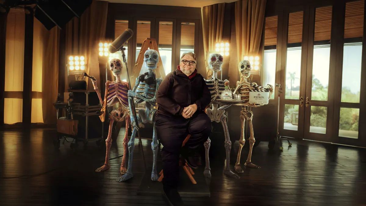 Filmmaker Guillermo del Toro sits on a chair, flanked by a team of skeletons