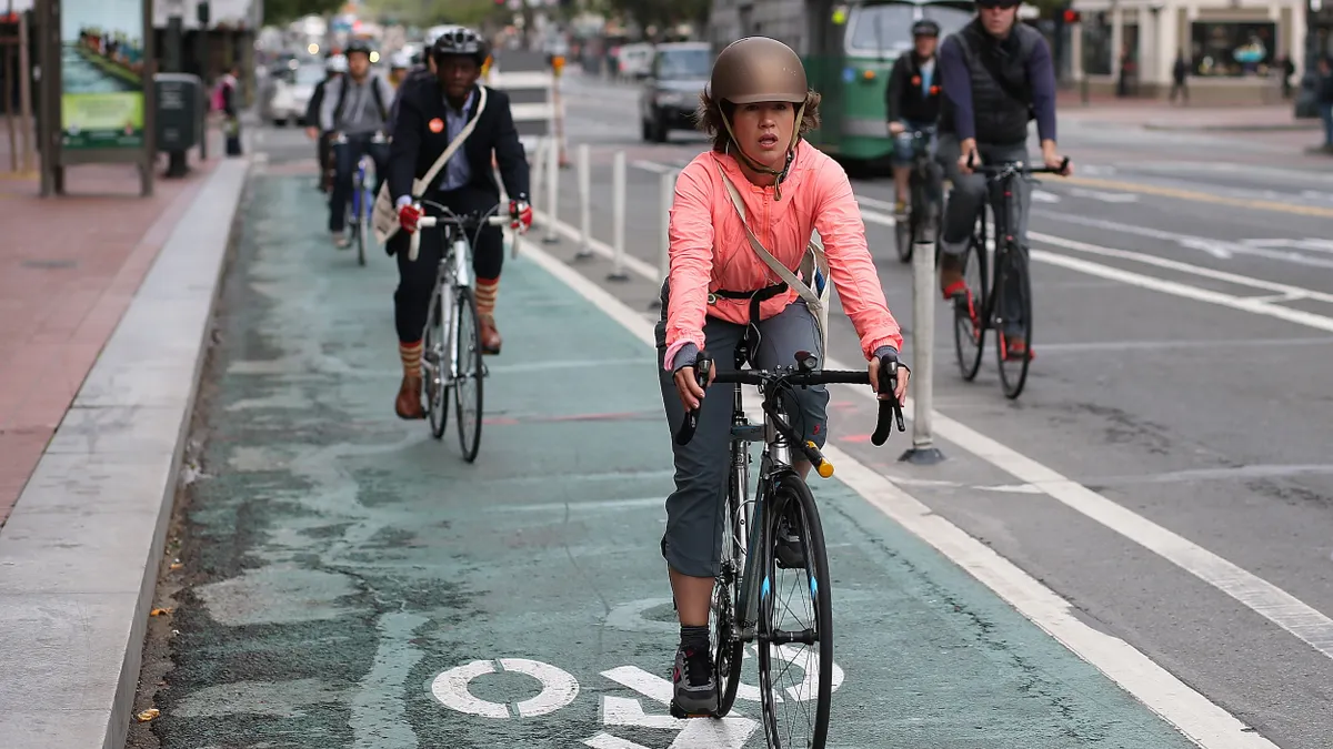 People riding bikes in a bike lane with cars and a bus on the main street.