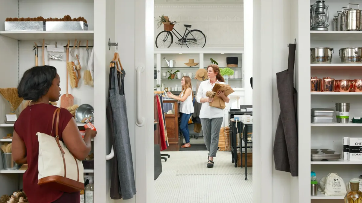 Three shoppers looking at different things in a brightly lit retail store.