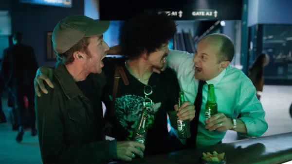 Three men with with their arms over each others shoulders while holding Heineken's.