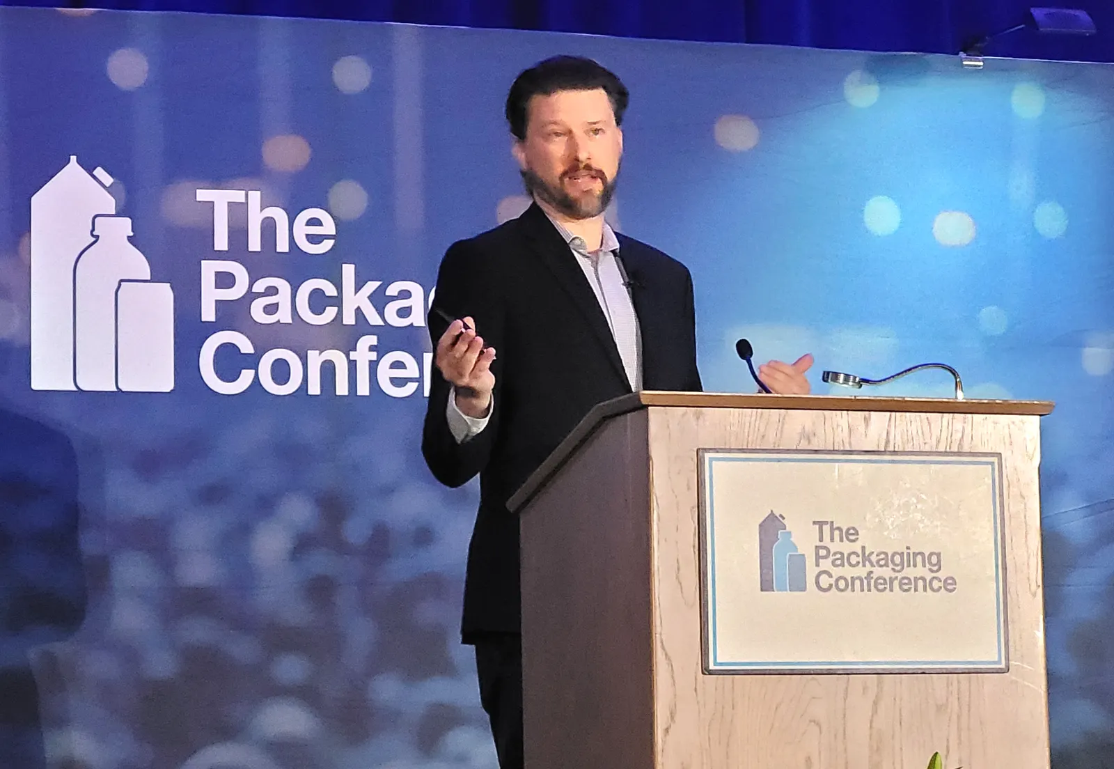 A person stands behind a podium with branding for The Packaging Conference on the podium.