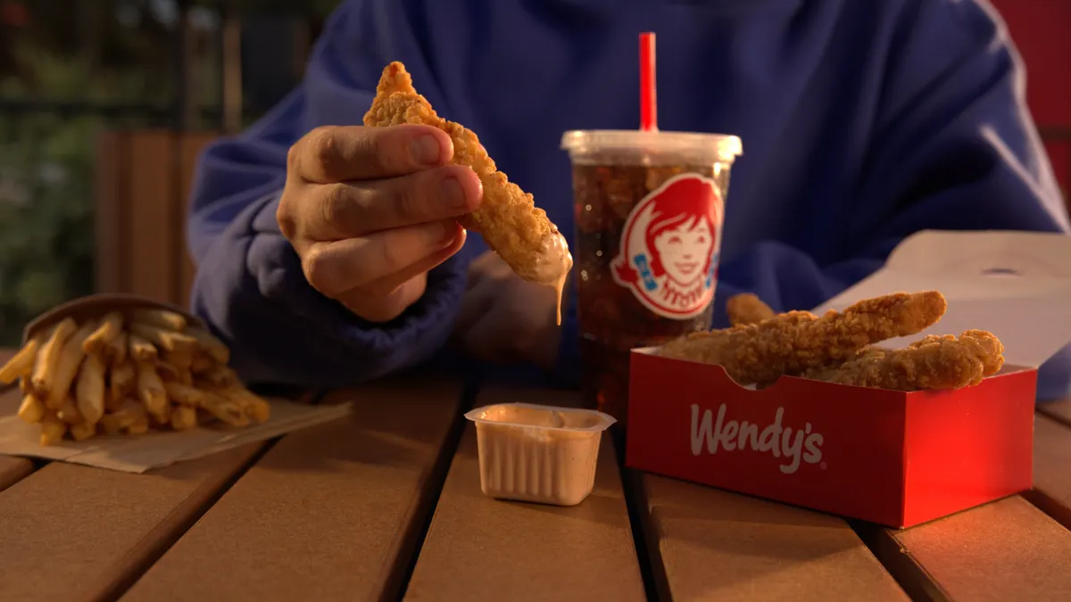 A hand dips a chicken tender into a sauce