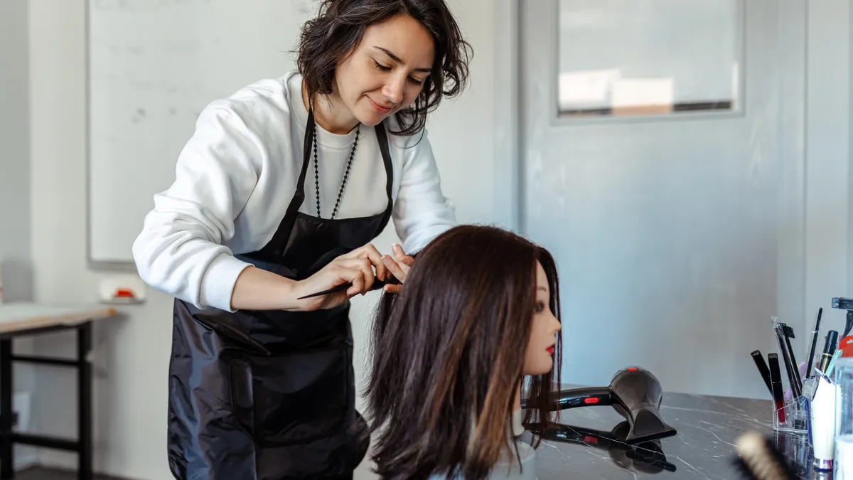 A beauty school student practices cutting and styling hair on a dummy.