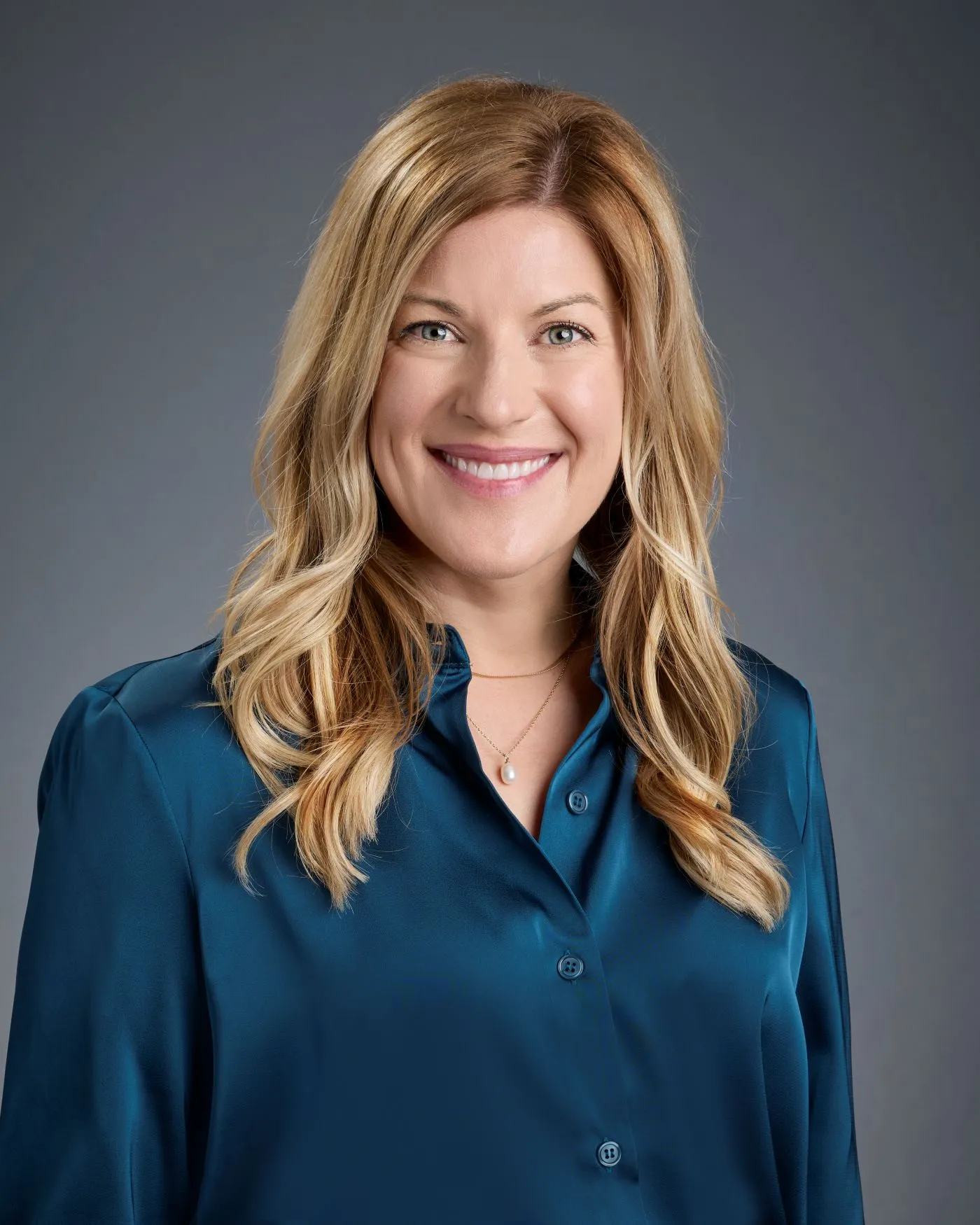 Headshot of a white woman with blonde hair wearing a blue button down against a charcoal gray backdrop