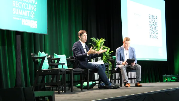 Two people sit in chairs on a stage in front of a banner saying Packaging Recycling Summit.