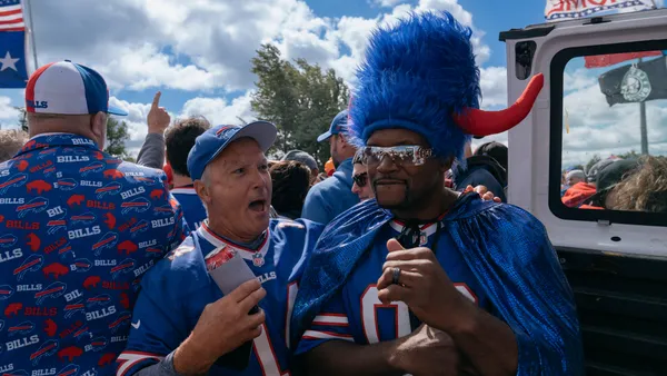 Anthony "Spice" Adams, wearing Buffalo Bills paraphernalia, stands next to a fan at a tailgate