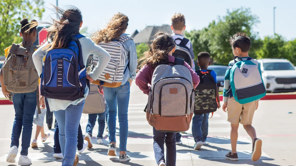 A group of students is walking outside carrying backpacks on their backs. Their backs are toward the camera.