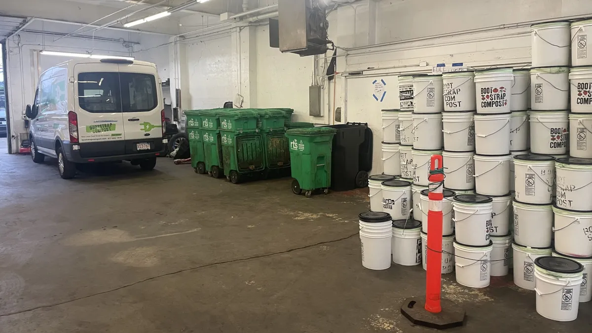 A view of Bootstrap Compost's electric van and a stack of white five-gallon buckets for organics collection