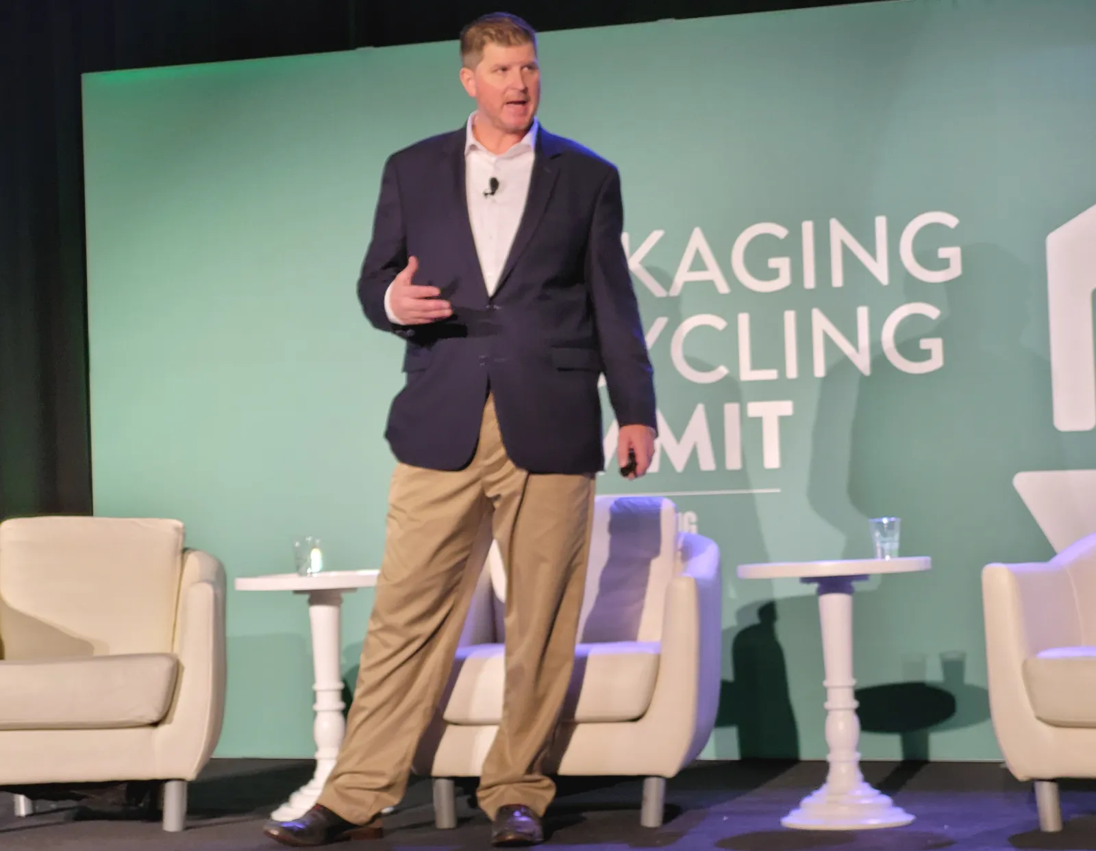 A person stands on a stage with a green background that says "Packaging Recycling Summit" in white letters.