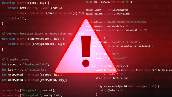 A computer monitor screen with code and a red exclamation point cyberattack warning visible.