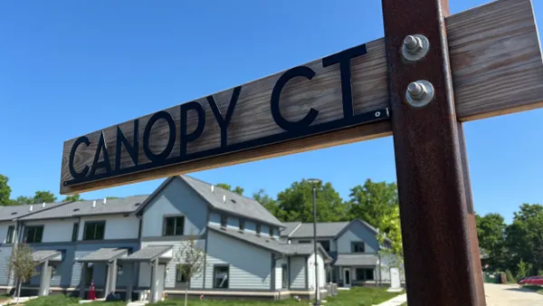 A wooden sign that says "Canopy Court" in front of new homes.