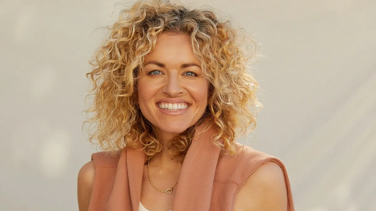 A headshot of a smiling person with curly blond hair