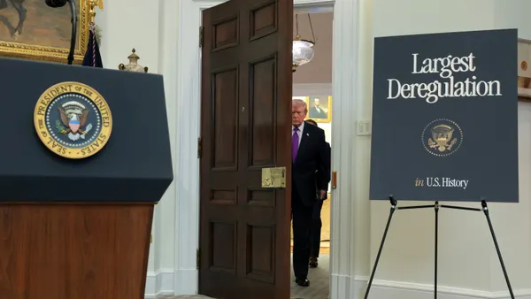 President Donald Trump walks into an ornate room where a podium is set up and a sign reads "Largest Deregulation in U.S. History."