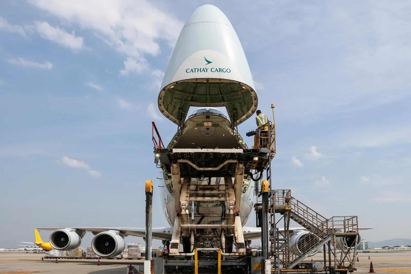 The nose of a Cathay Pacific cargo freighter is open with a cargo handler loading the aircraft.