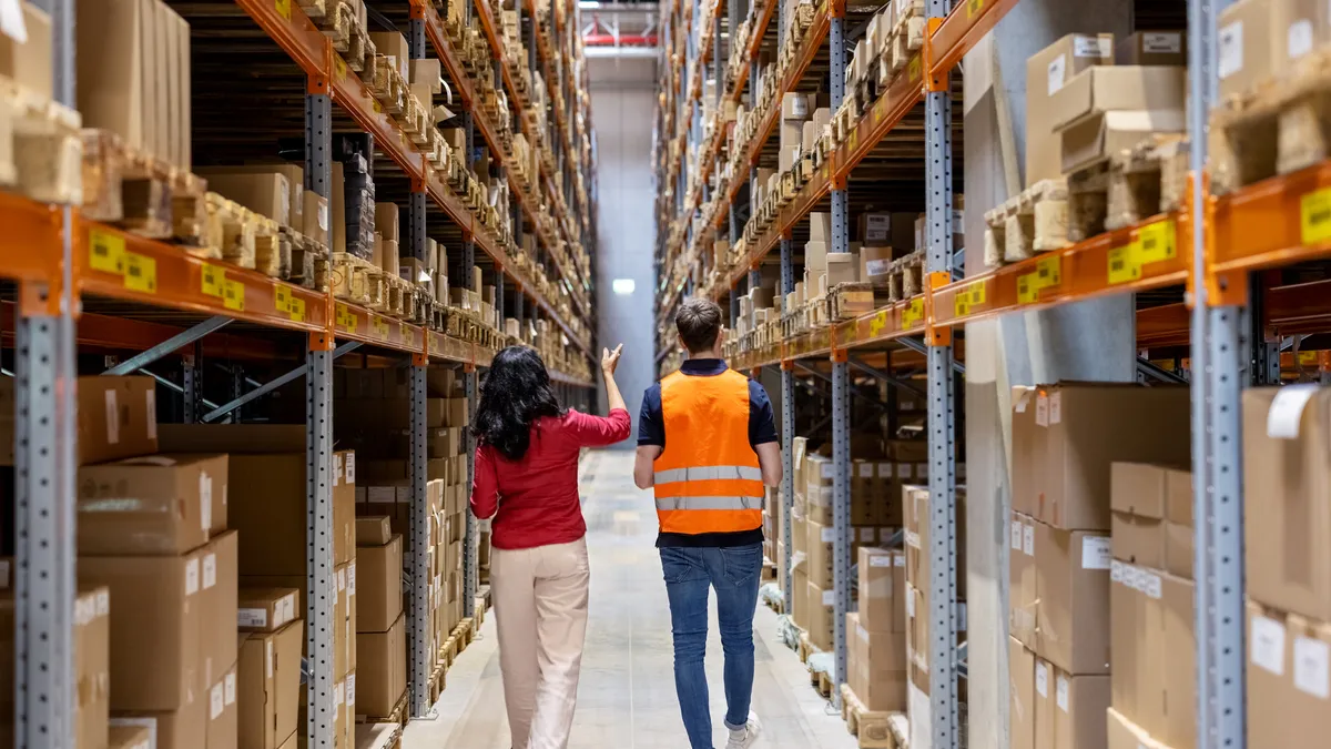 Rear view of a manager discussing stock with an employee at a supply chain warehouse.