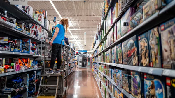 An employee uses a handheld device to check inventory in a retail toy aisle.