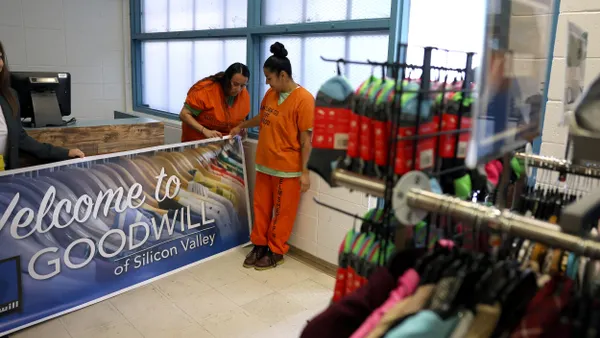 Two people in prison uniforms set up a Goodwill sign in a shop.
