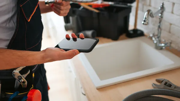 A person looks at their phone while repairing a sink.