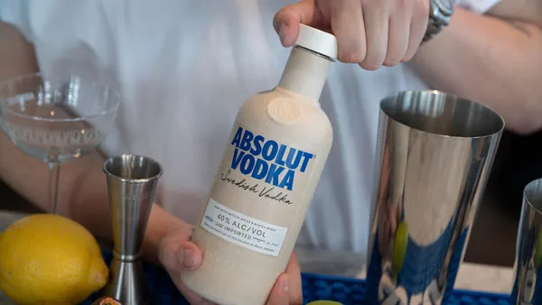 A person's hands open the paper-based cap on a paper-based bottle of Absolut Vodka.