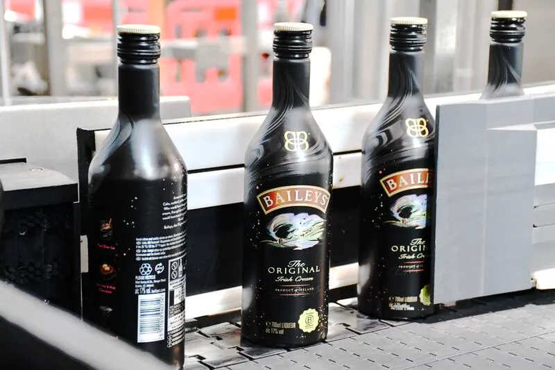 Bottles of Baileys irish cream alcoholic beverage in aluminum bottles on a manufacturing line.