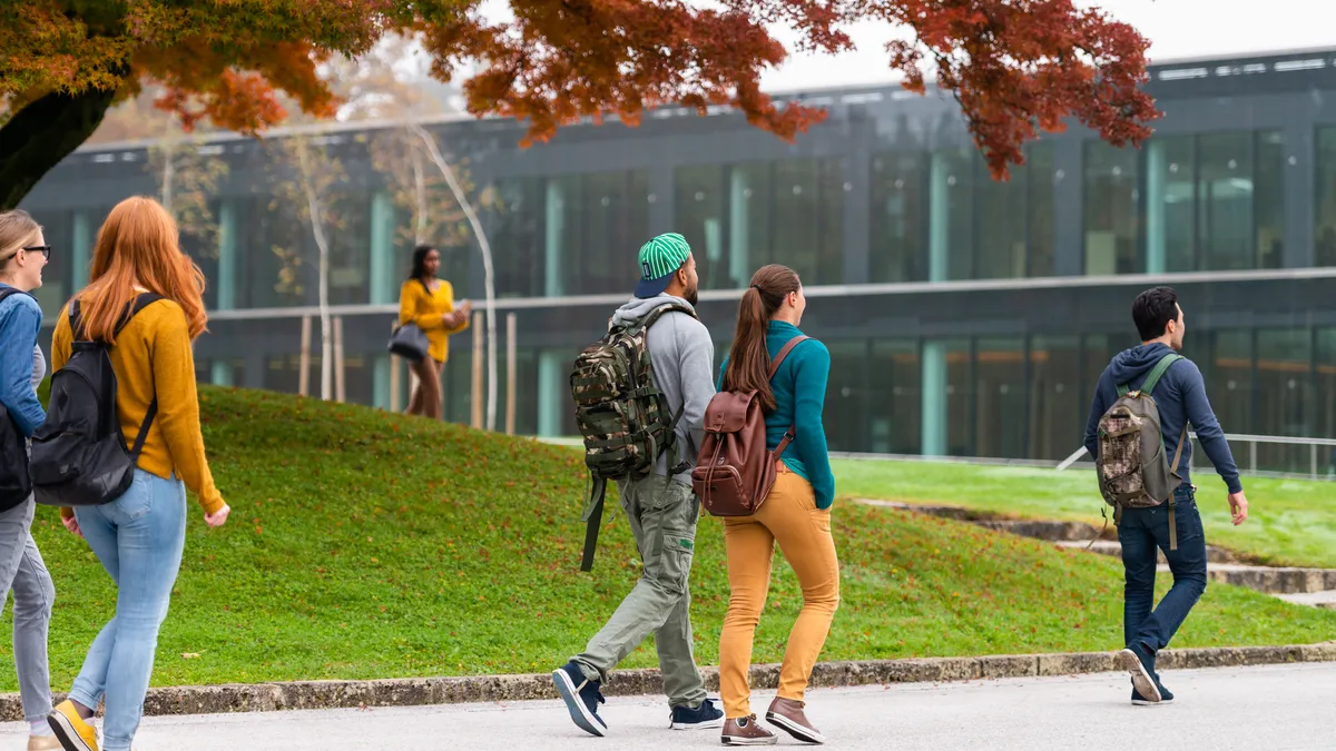 Group of students walking and standing in front of a modern glass university building