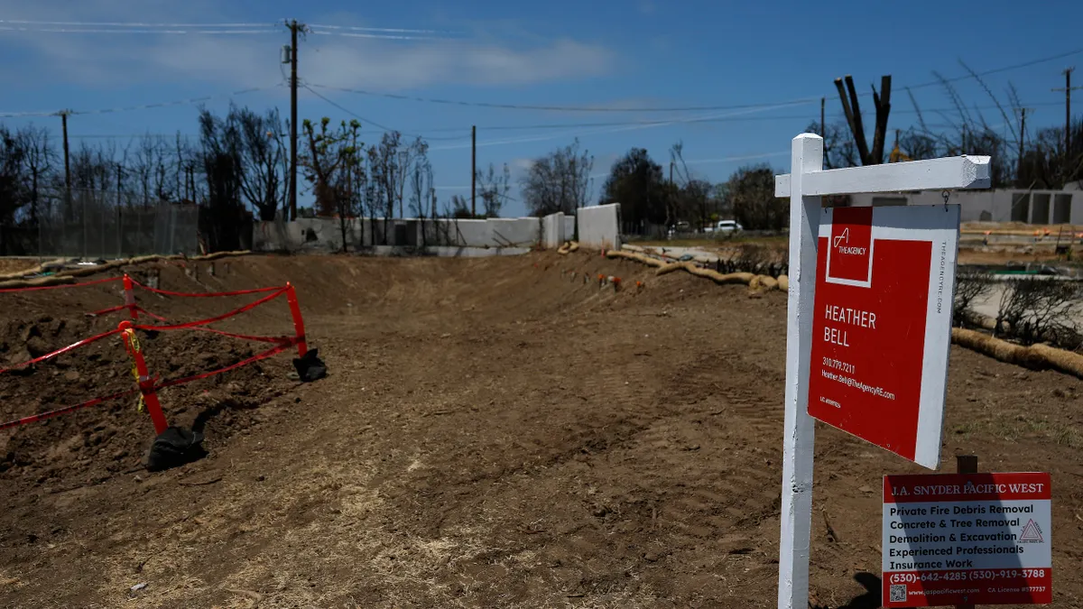 A red "For Sale" sign on a white post and a smaller sign about private fire debris removal in front of a bulldozed lot with burned trees in the background.