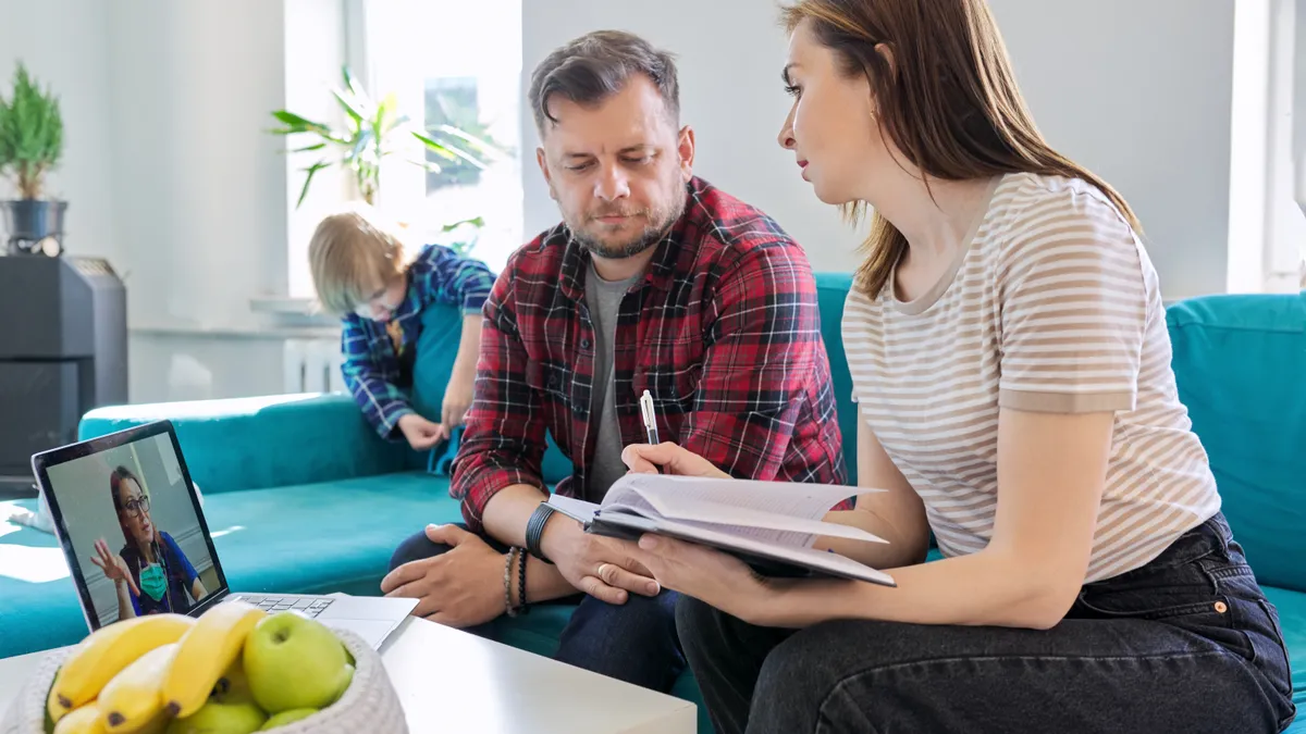 Telemedicine, technology, middle aged couple using laptop for video meeting with doctor. Husband and wife at home on the couch with child listening and talking to the doctor.